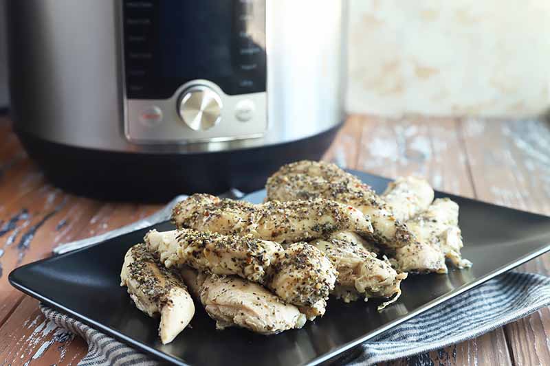 Horizontal image of seasoned white meat pieces on a black plate, with a kitchen appliance in the background.