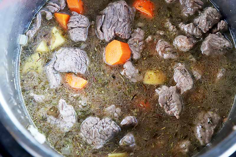 Horizontal image of stock, chunks of meat, and slices of vegetables in a pot.