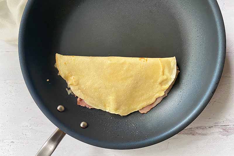 Horizontal image of a folding thin and filled pancake in a skillet.