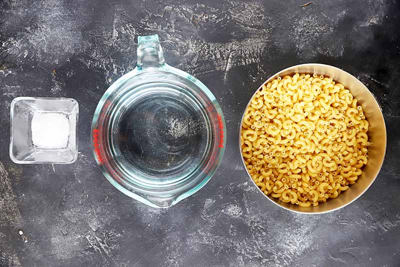 Horizontal image of a bowl of salt, a measuring cup of water, and a bowl of dried pasta.