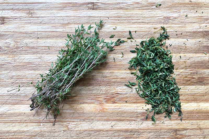 Horizontal image of piles of whole and chopped herbs on a wooden board.