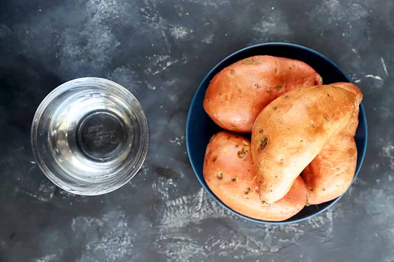 Horizontal image of a bowl of water and a bowl of whole unpeeled orange root vegetables.