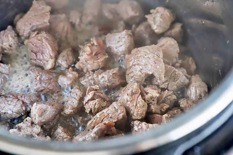 Horizontal image of browning chunks of meat in a pot.