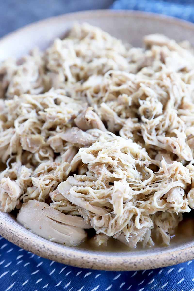 Vertical close-up image of a bowl of shredded chicken on a blue towel.