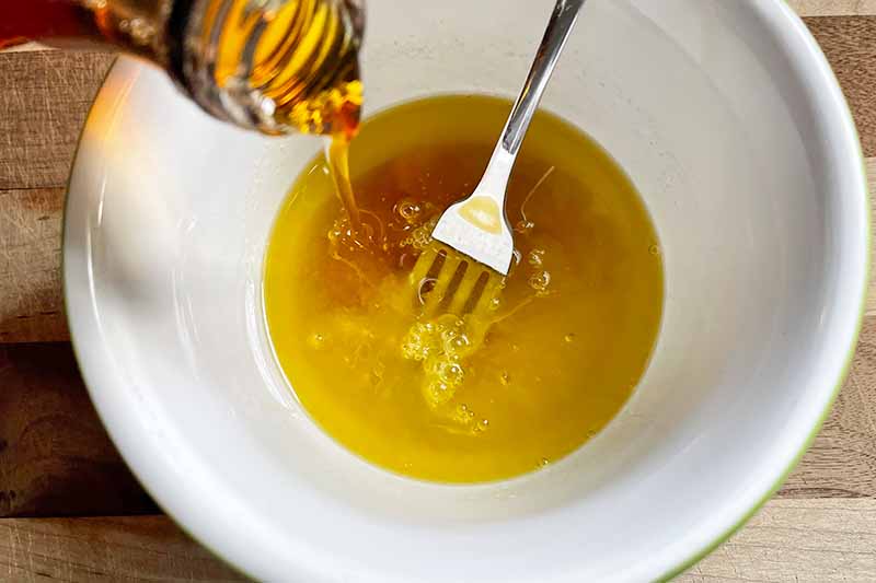 Horizontal image of pouring honey into a white bowl with a metal fork.