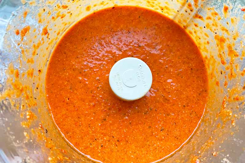 Horizontal image of a bright orange sauce in a food processor.
