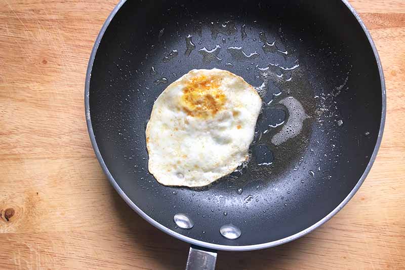 Horizontal image of an over-easy breakfast dish in a pan with oil.