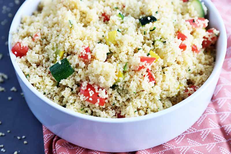 Horizontal image of a large white bowl filled with a mixed vegetable and couscous dish.