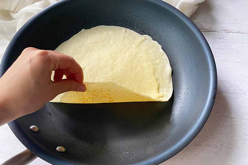 Horizontal image of a hand flipping over a cooked thin batter in a skillet.