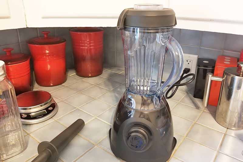 Horizontal image of a blender on a kitchen countertop with assorted containers.