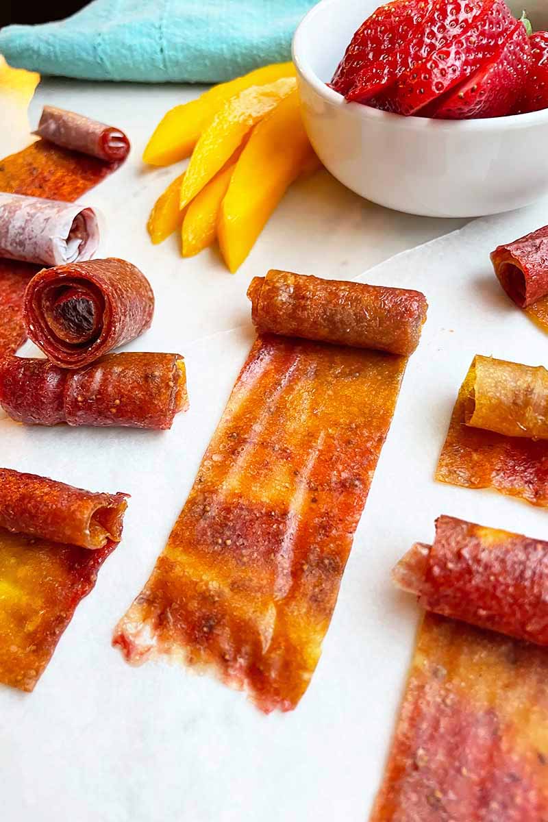 Vertical image of mango and strawberry rolls on a white surface next to a blue towel.