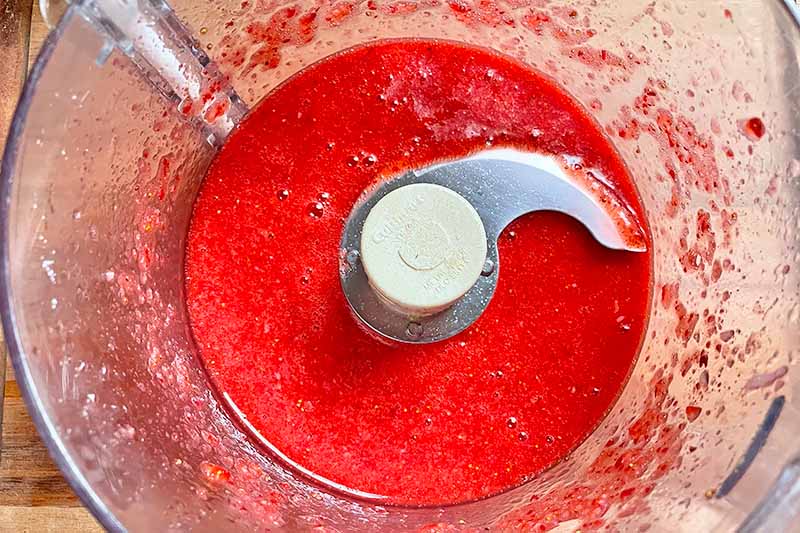 Horizontal image of a bright red puree in a food processor.