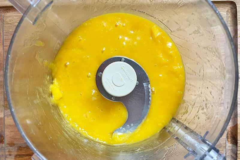 Horizontal image of a purred yellow mixture in a food processor.
