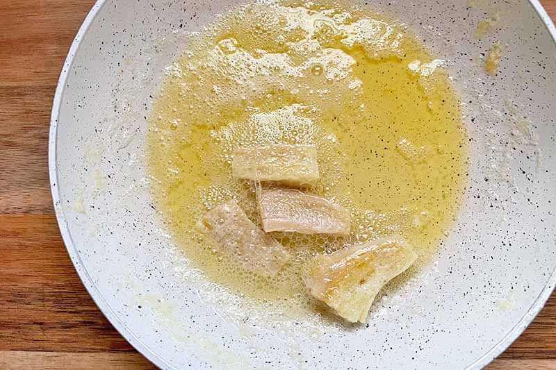 Horizontal image of butter and slices of ginger on a white bowl.