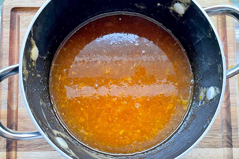Horizontal image of a bright orange liquid in a pot on a wooden cutting board.