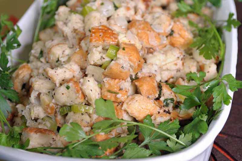 Horizontal image of bread stuffing with herbs in a white casserole dish.