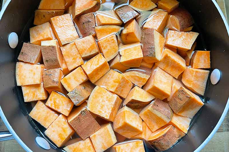Horizontal image of cubed sweet potatoes in water in a pot.