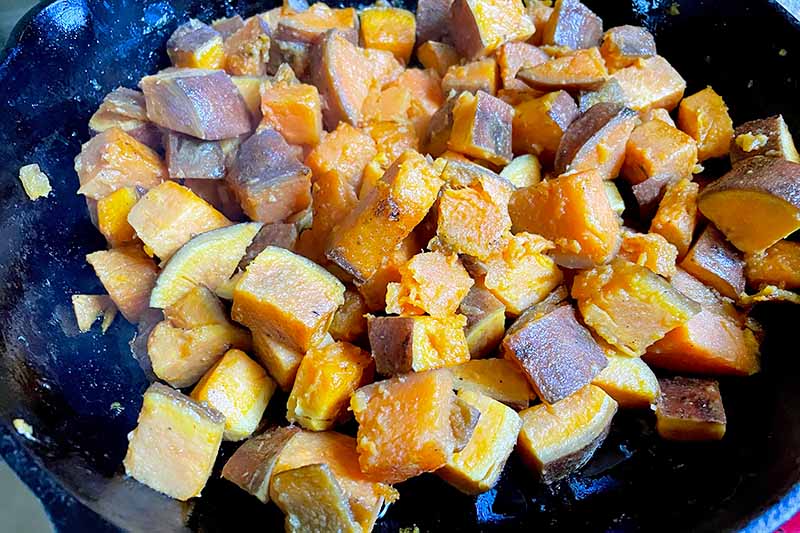 Horizontal image of cubed orange vegetables cooking in a cast iron skillet.