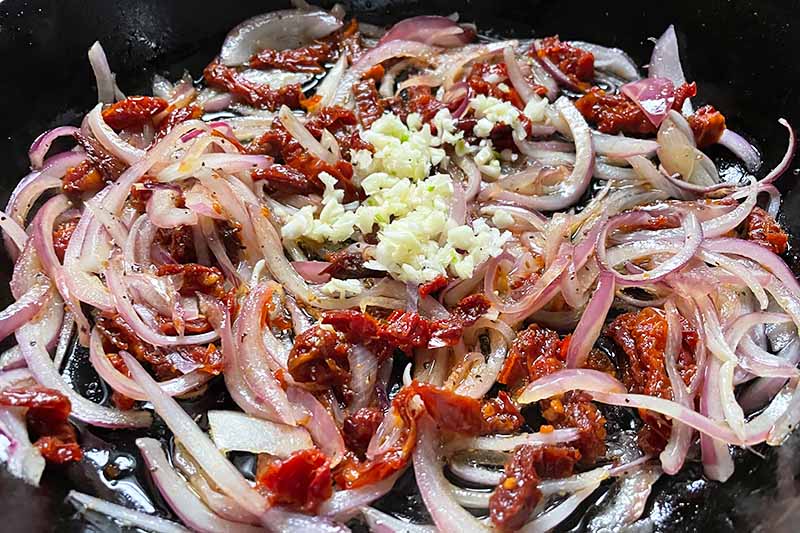 Horizontal image of cooking sliced red onions with minced garlic in a pan.