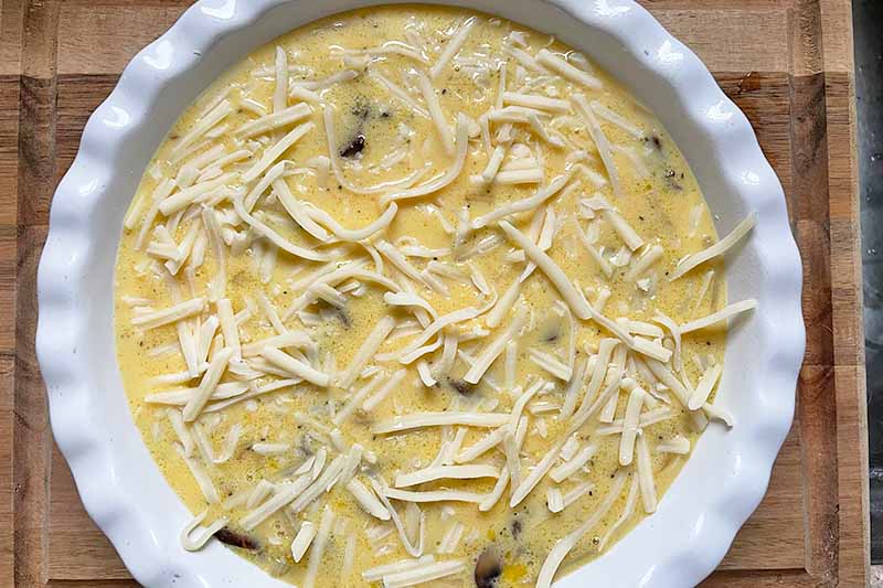 Horizontal image of raw eggs topped with cheese shreds in a white pie dish.
