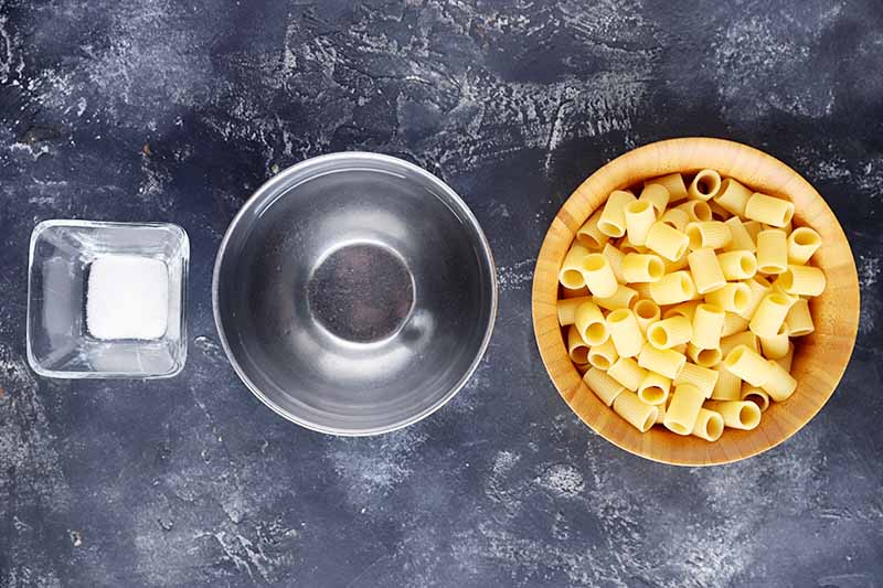 Horizontal image of salt, water, and rigatoni in bowls.