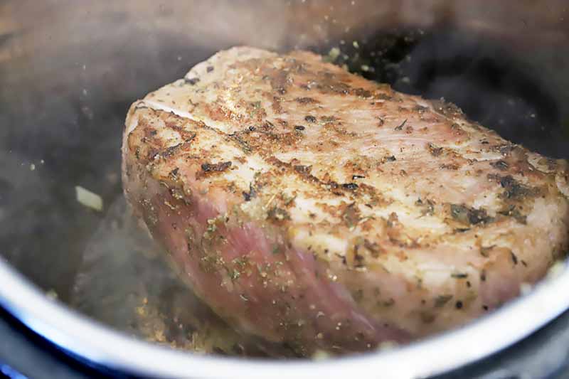 Horizontal image of searing a large piece of meat in a pot.