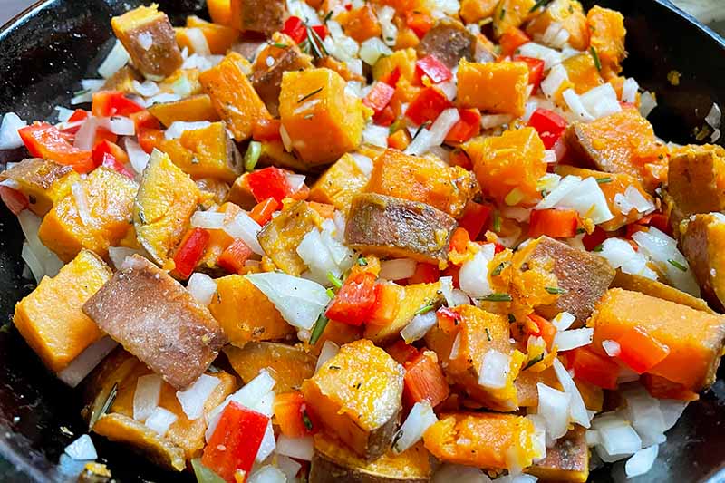 Horizontal image of cubed orange vegetables mixed with chopped peppers and onions in a pan.
