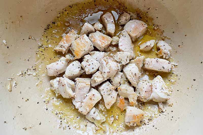 Horizontal image of searing pieces of poultry in oil in a pot.