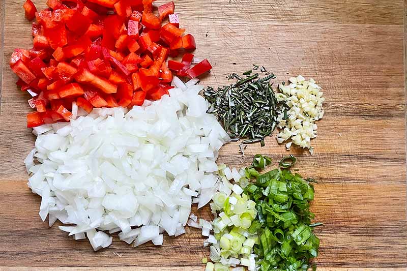 Horizontal image of chopped vegetables and seasonings on a wooden cutting board.
