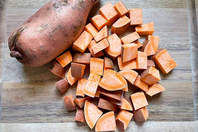 Horizontal image of cubed raw sweet potatoes on a wooden cutting board.
