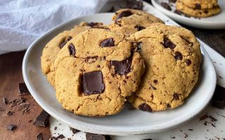 Horizontal image of a small mound of chocolate chunk cookies on a white plate on a cutting board.