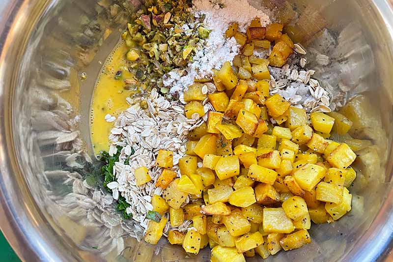 Horizontal image of dried ingredients and cubes of cooked squash in a metal mixing bowl.