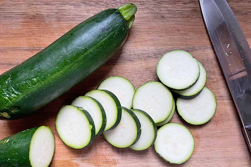 Horizontal image of whole and sliced green vegetables on a wooden cutting board next to a knife.