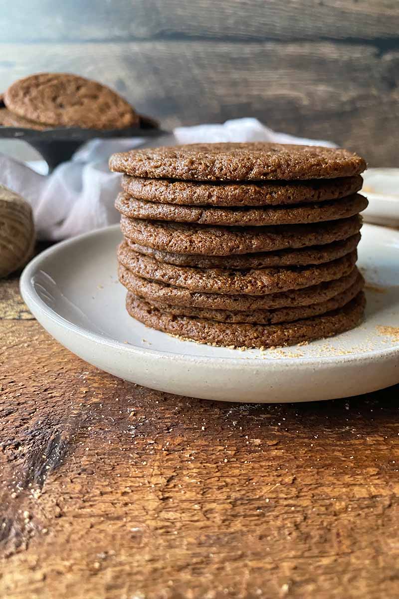 Vertical image of a tall stack of circular brown treats on a white plate on a wooden cutting board.