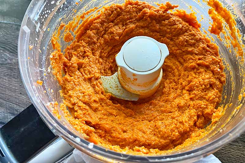 Horizontal image of a pureed thick orange mixture in a food processor.