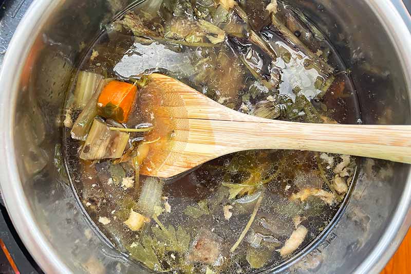 Horizontal image of a wooden spoon stirring soup in a metal pot.