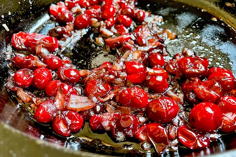 Horizontal image of cooking onions and cranberries in a pan.