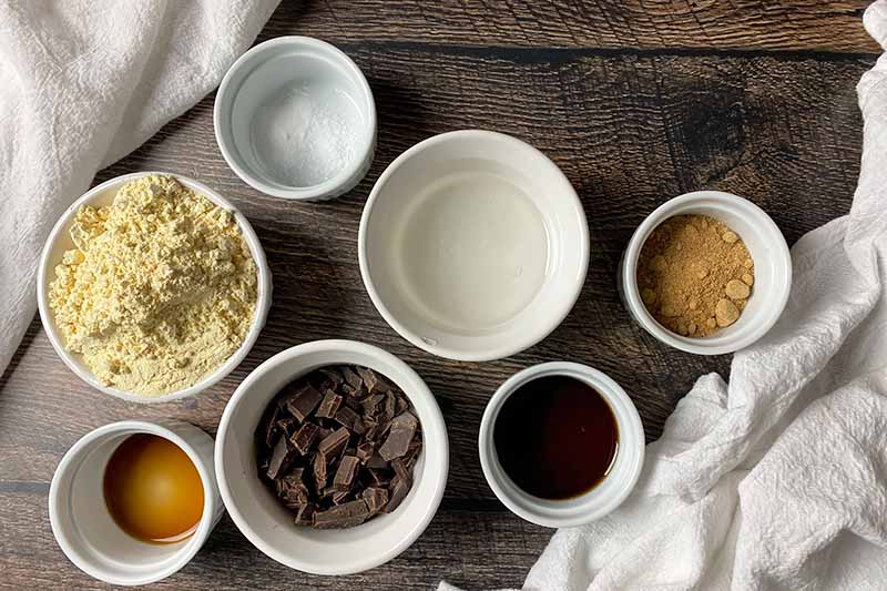 Horizontal image of assorted dry and wet ingredients in white bowls next to white towels.