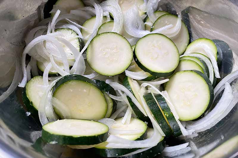 Horizontal image of slices of green vegetables and onions in a metal bowl.