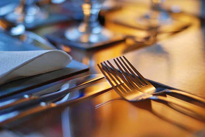 Horizontal image of silverware on a dimly lit table.