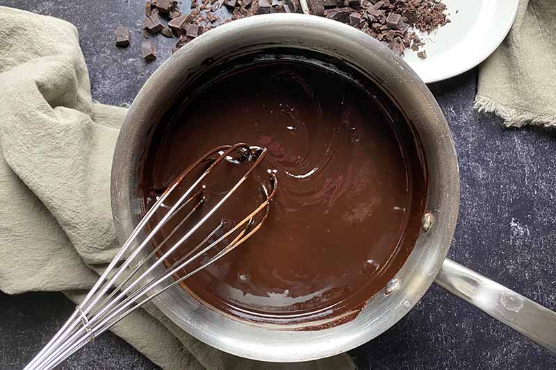 Horizontal image of whisking a dark brown smooth mixture in a pot next to tan towels.