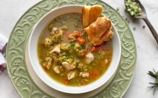 Horizontal image of a bowl of chunky green stew with a side of bread on a green plate.