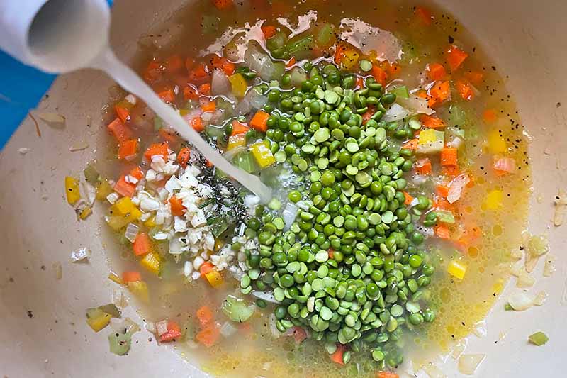 Horizontal image of mixing peas and broth in chopped vegetables in a pot.
