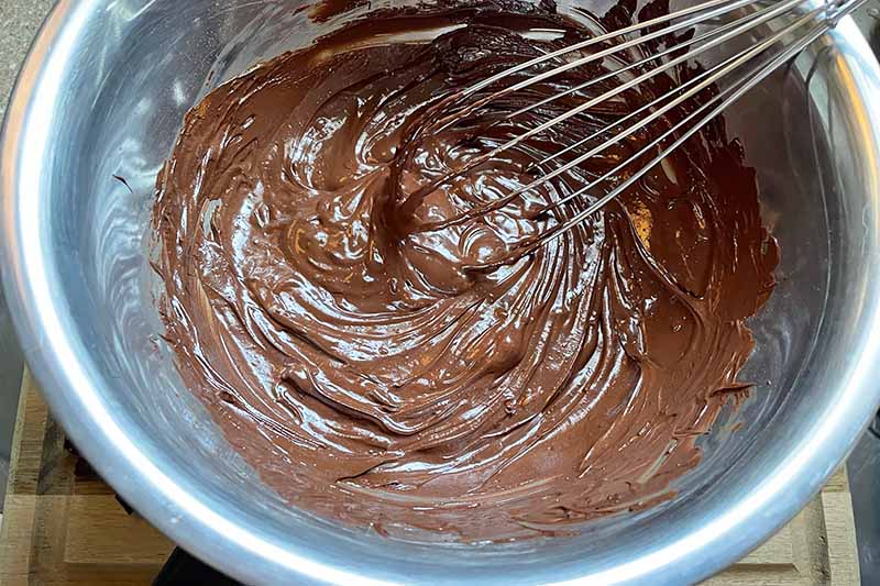 Horizontal image of melting chocolate in a metal bowl with a whisk.