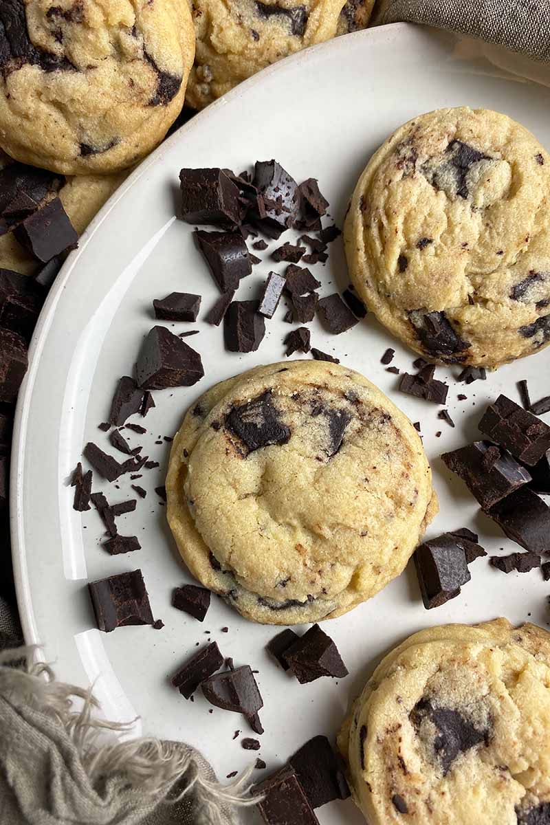 Vertical image of a white plate with cookies and dark brown candy chunks.