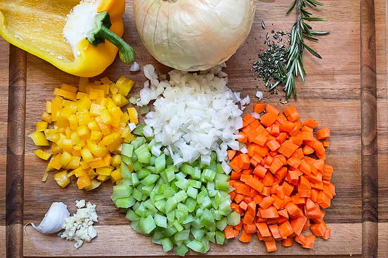 Horizontal image of assorted chopped vegetables in a wooden cutting board.
