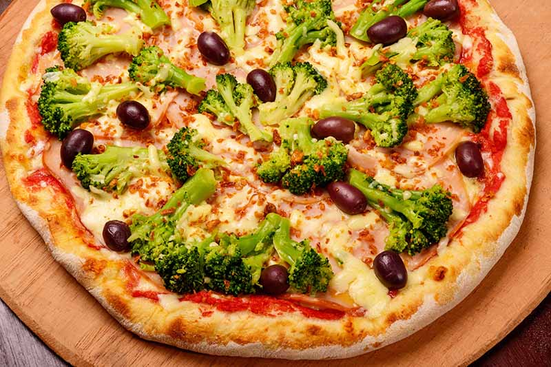 Horizontal image of broccoli and olives on a round flatbread.