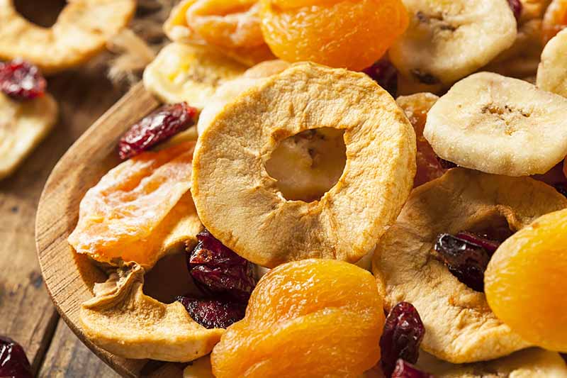 Horizontal image of dried apricots, bananas, apples, and cranberries on a wooden bowl.