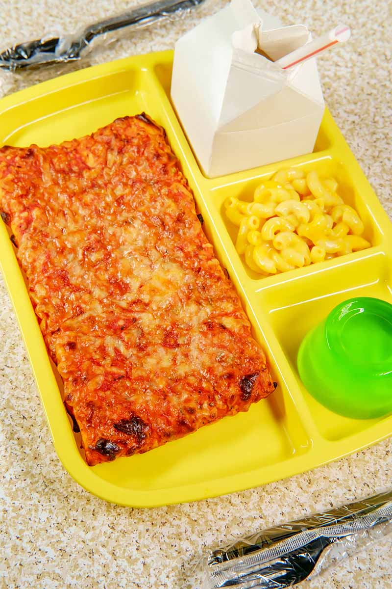 Vertical image of a yellow lunch tray with a cheese flatbread, jello, macaroni and cheese, and a milk carton.