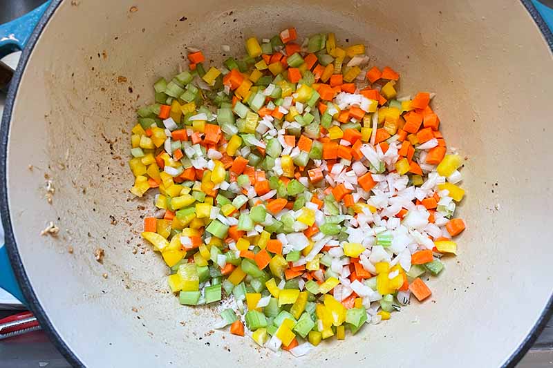 Horizontal image of assorted chopped vegetables cooking in a pot.